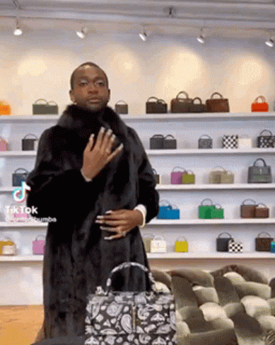 A Man Wearing A Fur Coat Is Standing In Front Of A Wall Of Bags . GIF