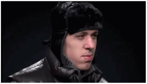 A Man Wearing A Fur Hat And A Leather Jacket Is Making A Funny Face . GIF