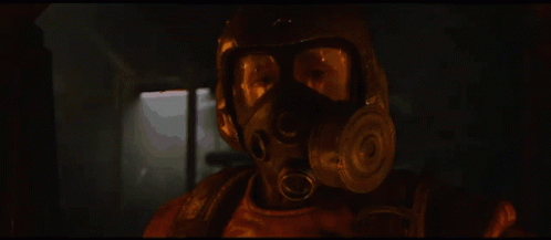 A Man Wearing A Gas Mask And Goggles Looks At The Camera With A Window In The Background GIF