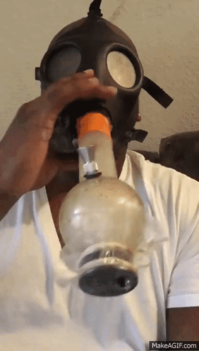 A Man Wearing A Gas Mask Is Blowing Smoke Out Of A Bong GIF