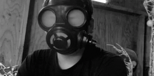 A Man Wearing A Gas Mask Looks At The Camera In A Black And White Photo GIF