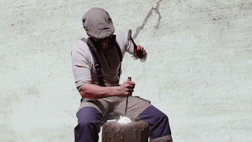 A Man Wearing A Gas Mask Sits In Front Of A Painting Of Hands Holding Money GIF