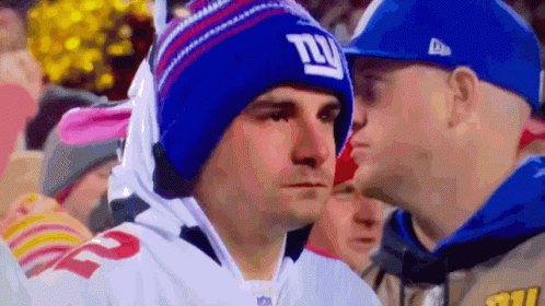 A Man Wearing A Giants Hat Looks At Another Man In A Blue Hat GIF