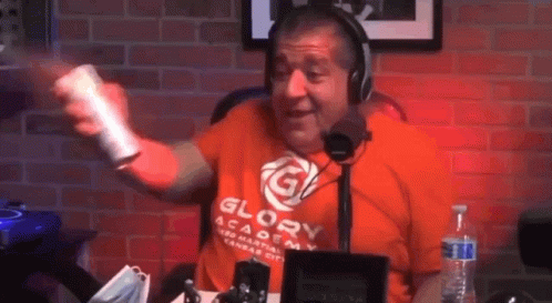 A Man Wearing A Glory Academy Shirt Is Holding A Remote Control In Front Of A Microphone . GIF