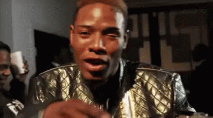 A Man Wearing A Gold Jacket Is Making A Funny Face . GIF