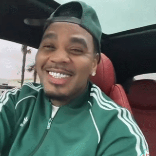 A Man Wearing A Green Adidas Jacket And A Green Hat Is Smiling While Sitting In A Car . GIF