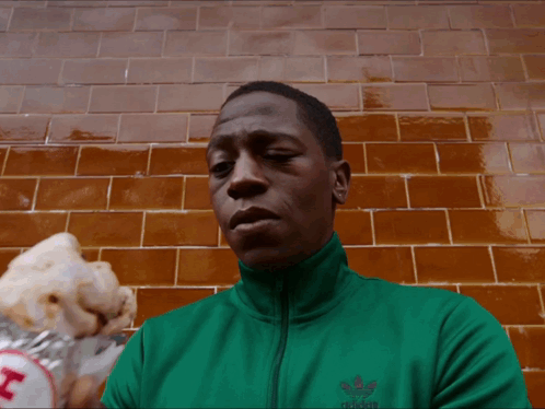 A Man Wearing A Green Adidas Jacket Eating A Hot Dog GIF