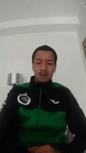 A Man Wearing A Green And Black Jacket Is Making A Face . GIF