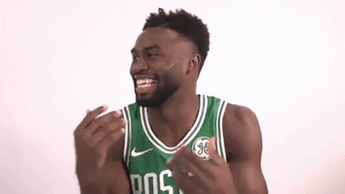 A Man Wearing A Green And White Boston Celtics Jersey Is Laughing With His Hands In The Air . GIF