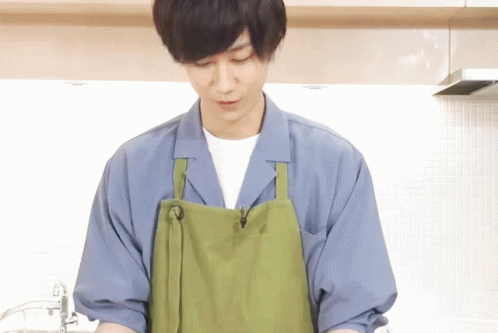 A Man Wearing A Green Apron And A Blue Shirt Is Cooking In A Kitchen GIF