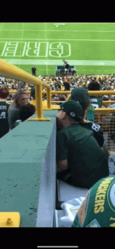 a man wearing a green bay packers jersey sits on a bleacher