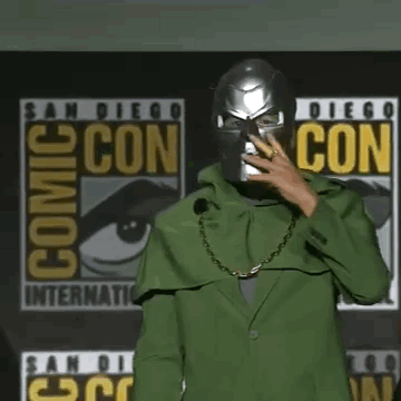 A Man Wearing A Green Cape And A Chain Around His Neck Is Standing In Front Of A Microphone . GIF