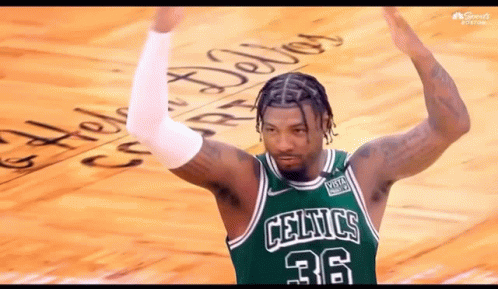 A Man Wearing A Green Celtics Jersey Is Standing On A Court With His Arms In The Air . GIF