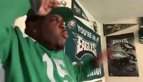 A Man Wearing A Green Eagles Jersey Is Standing In Front Of A Wall . GIF