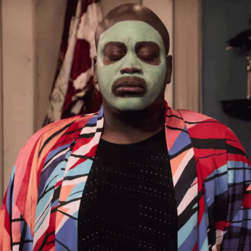 A Man Wearing A Green Face Mask And A Colorful Robe GIF