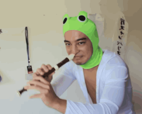 A Man Wearing A Green Frog Hat Is Holding A Flute GIF