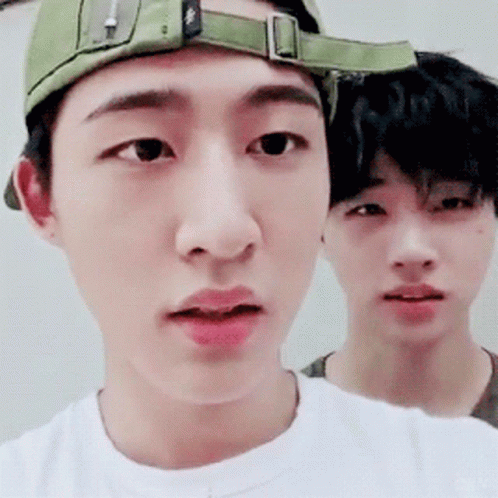 A Man Wearing A Green Hat And A White Shirt Is Standing Next To Another Man GIF