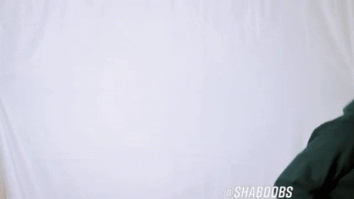 A Man Wearing A Green Hoodie Is Dancing In Front Of A White Wall . GIF