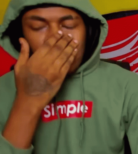 A Man Wearing A Green Hoodie With The Word Simple On It Covering His Mouth With His Hand . GIF