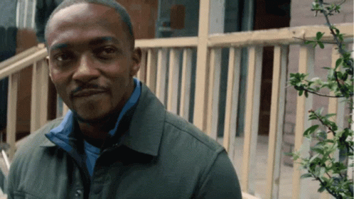 A Man Wearing A Green Jacket And A Blue Shirt Is Standing In Front Of A Railing GIF