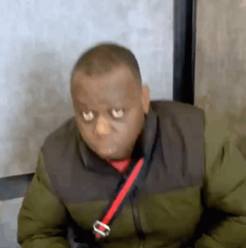 A Man Wearing A Green Jacket And A Red Tie Is Sitting In A Chair . GIF