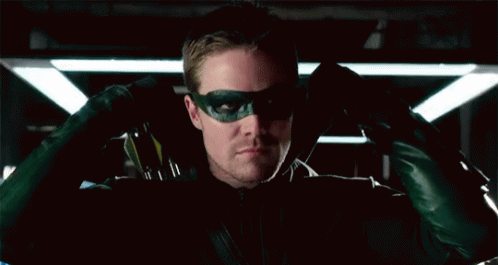 A Man Wearing A Green Mask And Gloves Is Sitting In A Dark Room . GIF