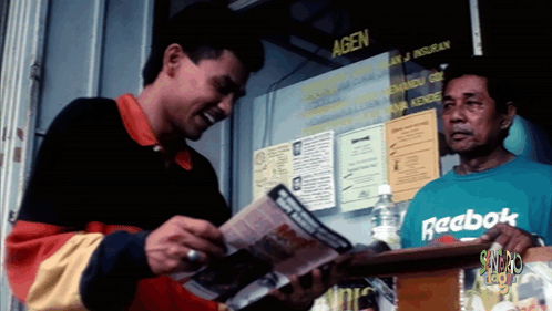 A Man Wearing A Green Reebok Shirt Stands In Front Of A Window GIF