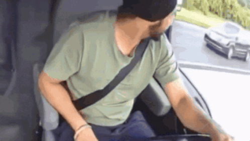 A Man Wearing A Green Shirt And A Black Hat Is Sitting In The Driver 'S Seat Of A Car GIF
