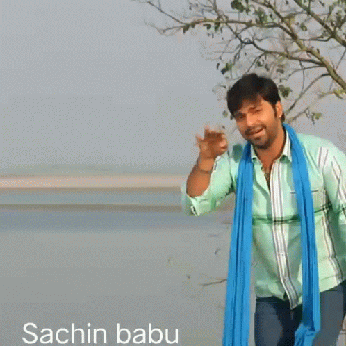 a man wearing a green shirt and a blue scarf stands in front of a body of water