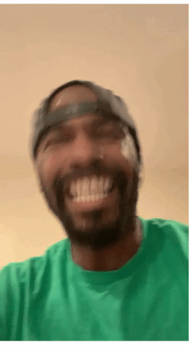 A Man Wearing A Green Shirt And A Hat Smiles GIF
