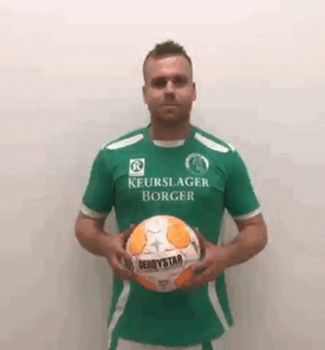 a man wearing a green shirt is holding a soccer ball .