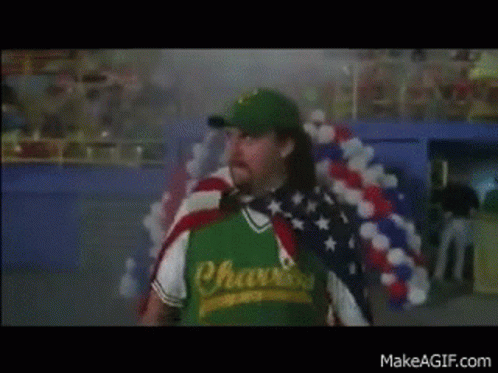 A Man Wearing A Green Shirt That Says Chasers Is Holding An American Flag Around His Neck . GIF