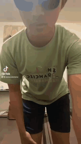 A Man Wearing A Green T-Shirt And Black Shorts Is Standing In A Room . GIF