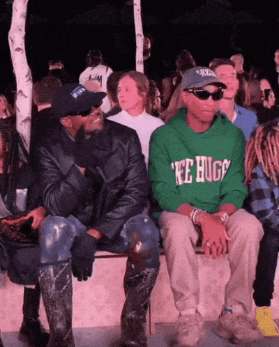 A Man Wearing A Green Tee Hugs Sweatshirt Sits Next To A Man Wearing A Black Jacket GIF