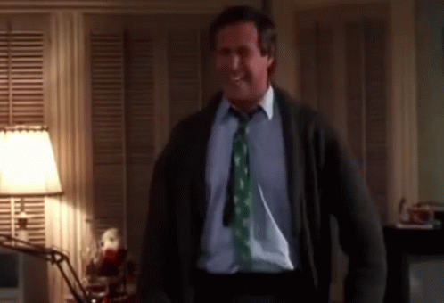 A Man Wearing A Green Tie And A Sweater Is Standing In A Room GIF