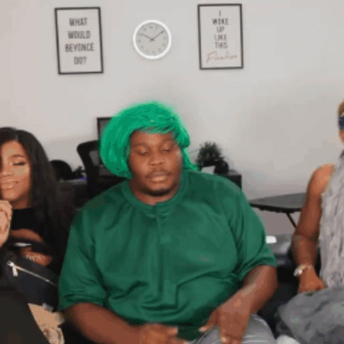 a man wearing a green wig and a green shirt is sitting on a couch with two women .