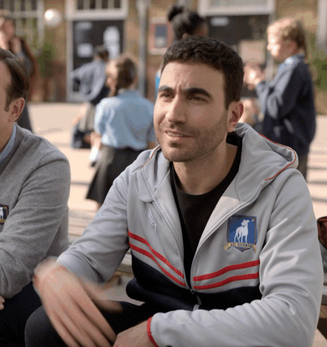 A Man Wearing A Grey Jacket With A Shield That Says Rugby League On It GIF