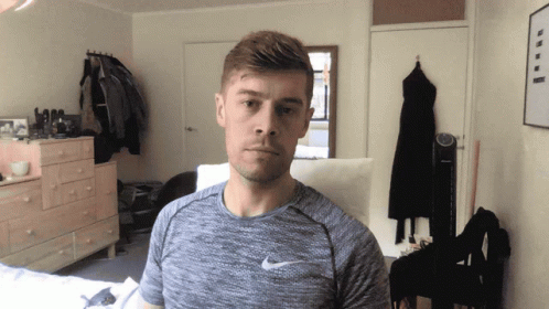 A Man Wearing A Grey Nike Shirt Stands In A Room GIF