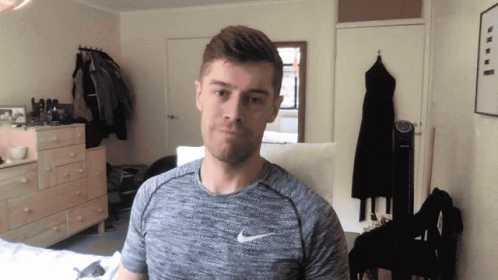 A Man Wearing A Grey Nike Shirt Stands In A Room GIF