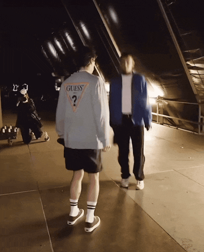 A Man Wearing A Guess Sweater Is Walking With Another Man GIF