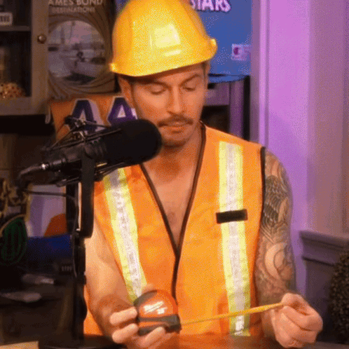 A Man Wearing A Hard Hat And Safety Vest Is Measuring Something With A Tape Measure GIF