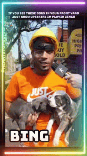 A Man Wearing A Hard Hat Is Holding Two Dogs And Talking Into A Microphone With The Word Bing On The Bottom GIF