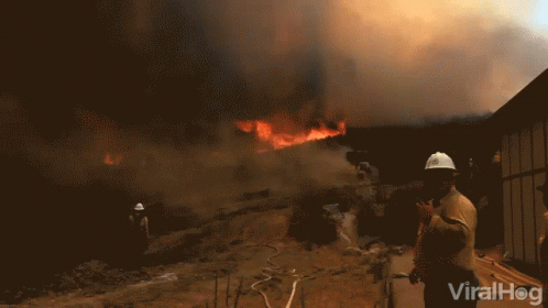 A Man Wearing A Hard Hat Stands In Front Of A Fire With The Words Viralhog Written On The Bottom GIF