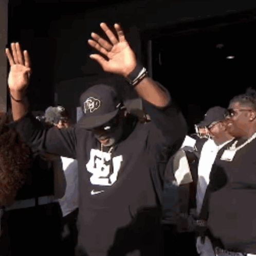 A Man Wearing A Hat And A Black Shirt With The Letter S On It GIF