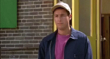 A Man Wearing A Hat And A Blue Jacket Is Standing In Front Of A Brick Building . GIF
