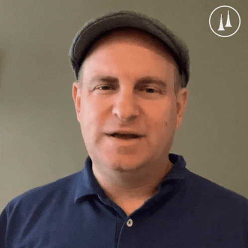 A Man Wearing A Hat And A Blue Shirt Is Looking At The Camera GIF