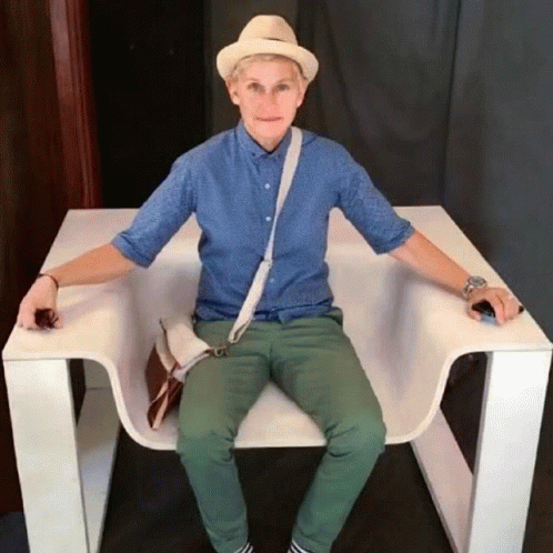 A Man Wearing A Hat And A Blue Shirt Is Sitting In A White Chair GIF