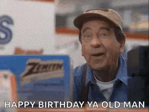 A Man Wearing A Hat And A Blue Shirt Is Standing In Front Of A Sign That Says Happy Birthday Ya Old Man . GIF