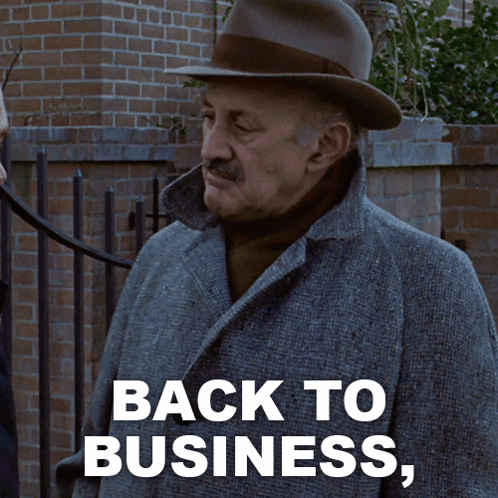 A Man Wearing A Hat And A Coat Says " Back To Business " GIF