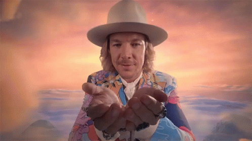 A Man Wearing A Hat And A Colorful Suit Is Holding His Hands Out GIF